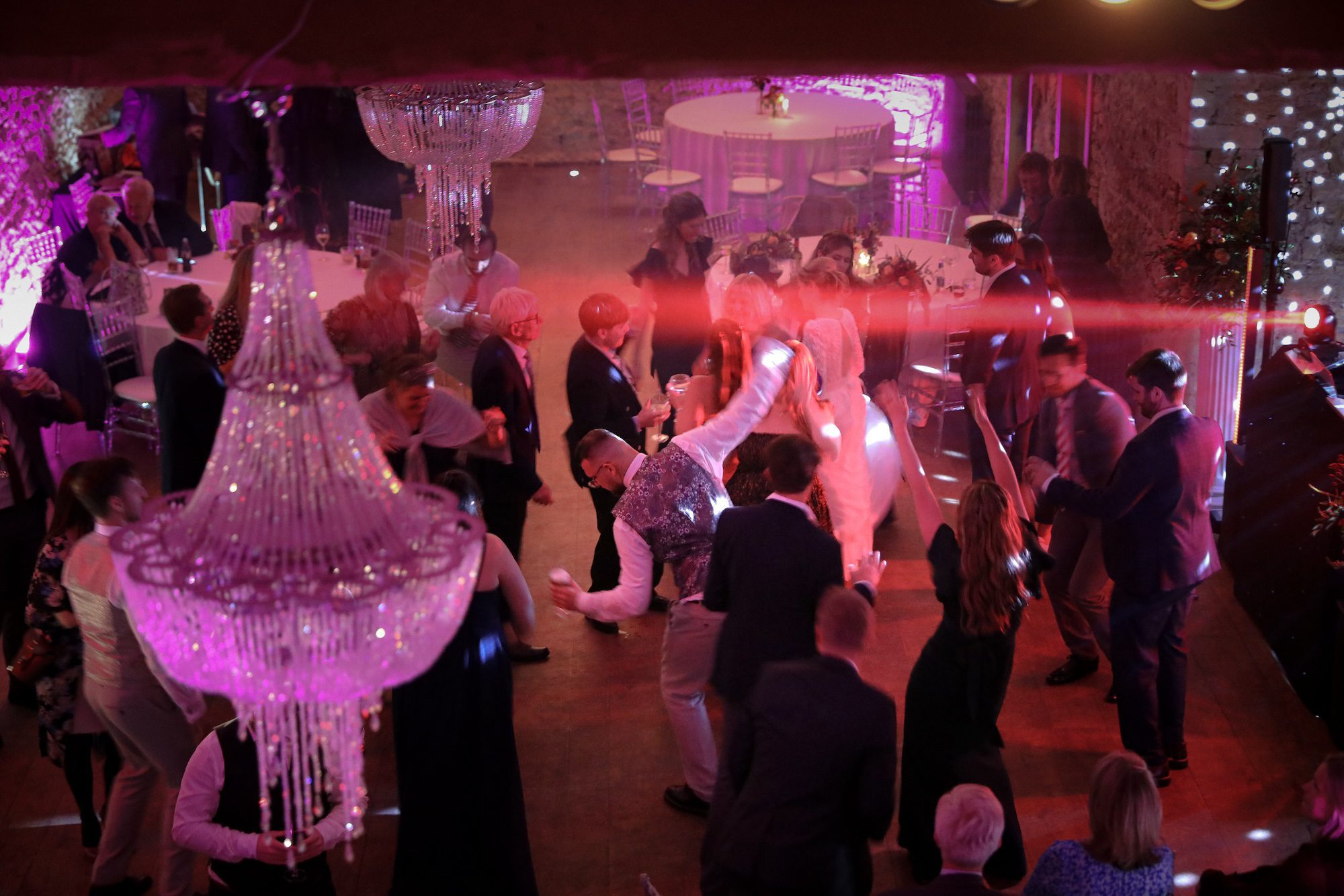 Wedding guests dance beneath chandeliers at the evening party in the stone barn at Notley Abbey, Buckinghamshire