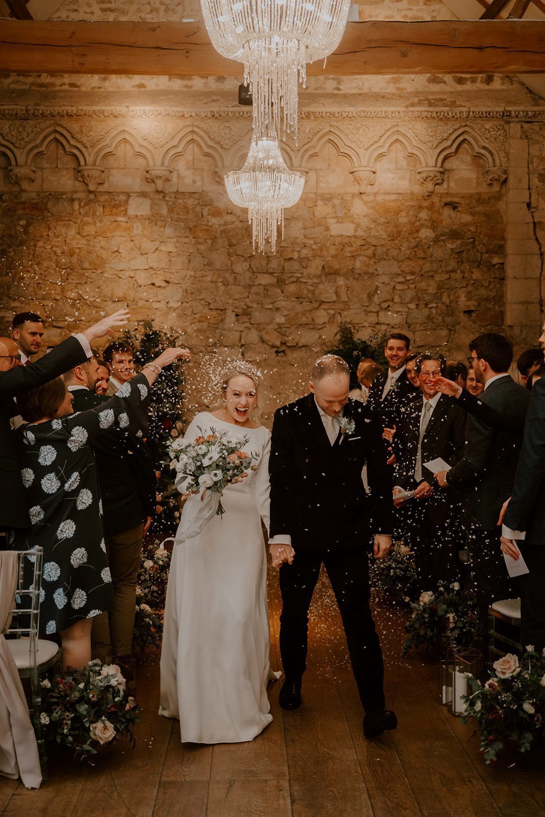Newlyweds walk back down the aisle under confetti in the Monks' Refectory at Notley Abbey, Buckinghamshire