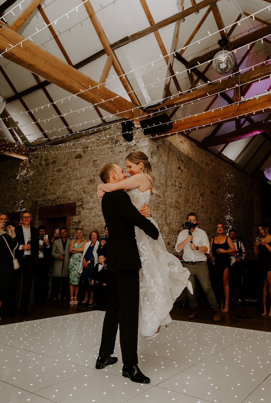 Groom lifts the bride during their first dance in the stone barn at Notley Abbey, Buckinghamshire wedding venue